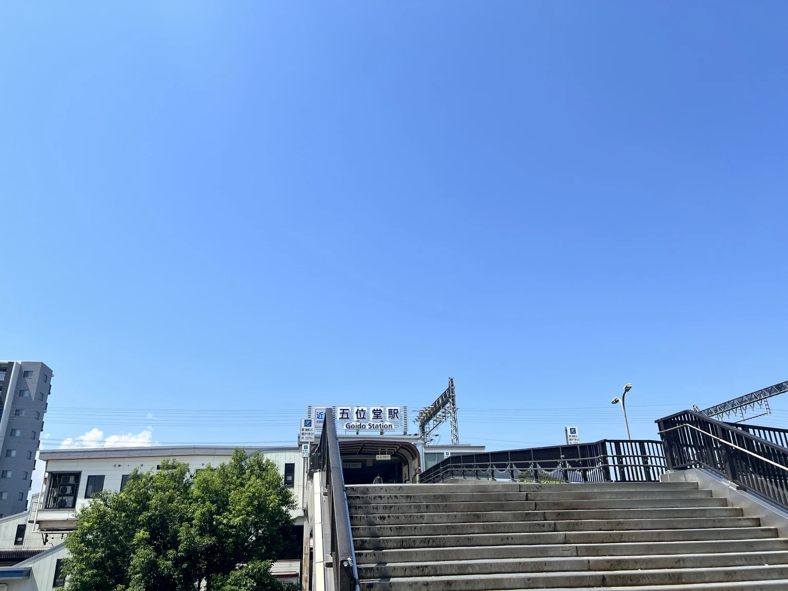 青空の下、近鉄五位堂駅の駅舎と歩道橋を正面から見た風景